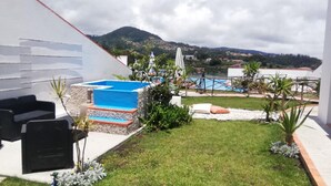 Ein Poolbereich mit blauem Pool, Sitzgelegenheiten im Freien und Blick auf eine gebirgige Landschaft.