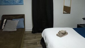 Ein Schlafzimmer mit Bett, Schreibtisch, Stuhl, schwarzem Vorhang, Spiegel und einem blauen Bild an der Wand.