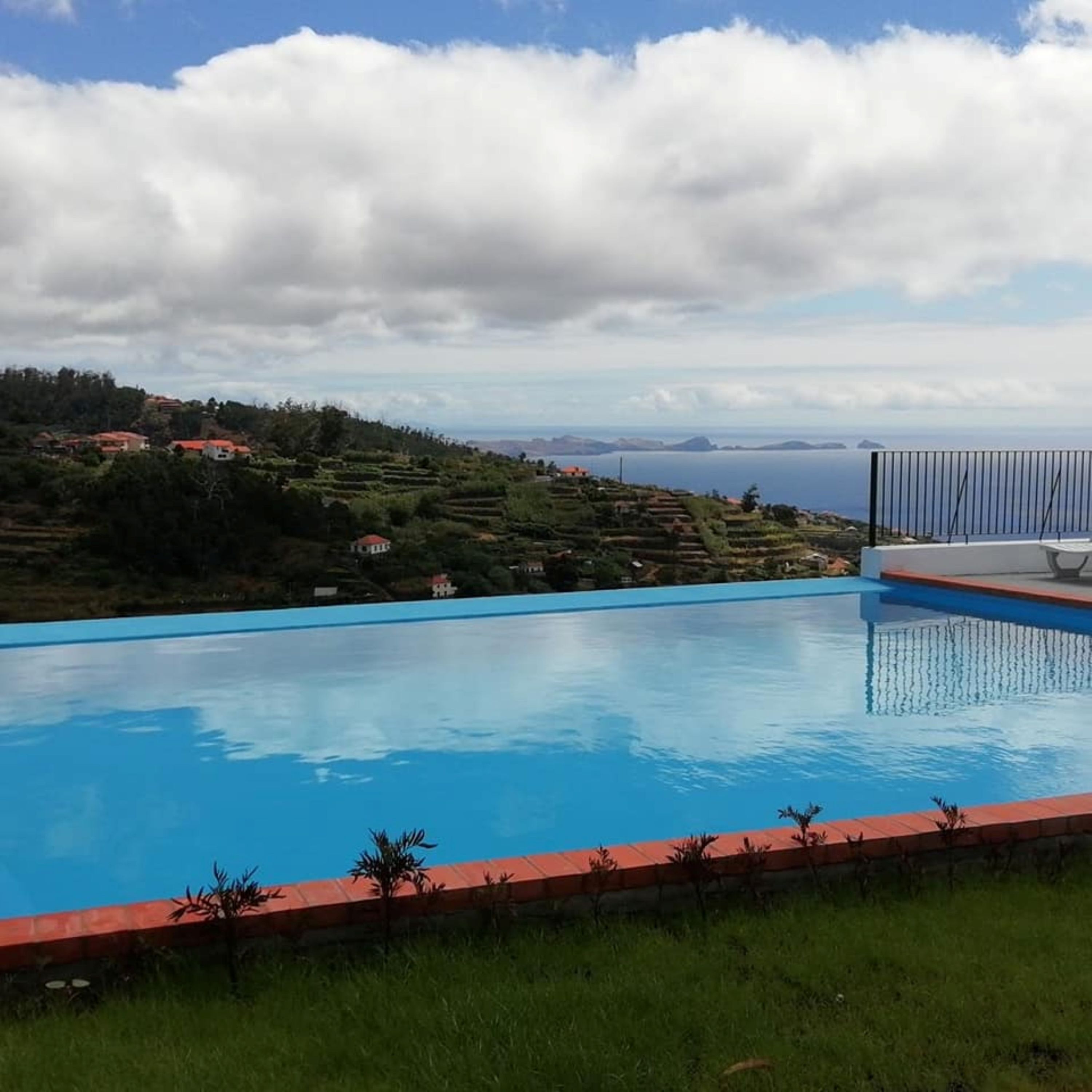 A swimming pool with a view of a coastal landscape and distant islands.