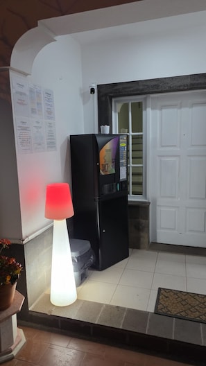 Ein Zimmer mit einem schwarzen Kühlschrank, einer roten und weißen Lampe, einer weißen Tür und einem Fenster mit Jalousien.