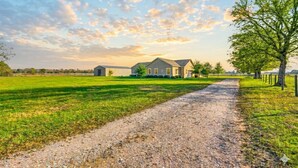 A gravel path leading to a house with a large lawn and trees. - Luxurious Farm Stay Near Houston  -  5BR Gated Acreage (Waller)