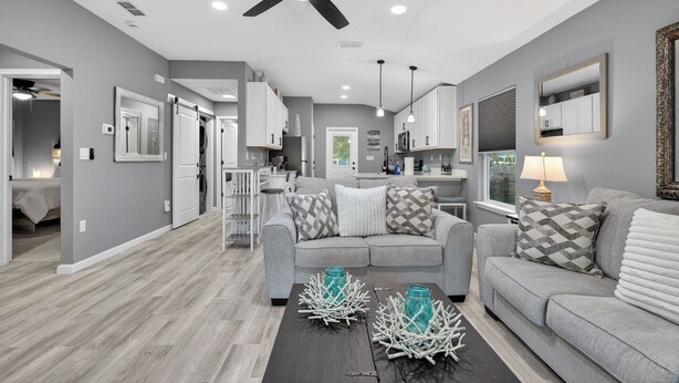 A modern living room with a grey sofa, a coffee table with decorative items, and a ceiling fan. - Welcome Home! 2-bedroom house in lovely St. Augustine with cool AC (St. Augustine)