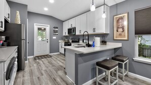 A modern kitchen with grey walls, white cabinets, a central island, and bar stools. - Welcome Home! 2-bedroom house in lovely St. Augustine with cool AC (St. Augustine)