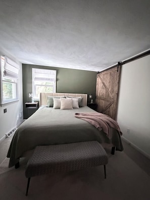 Une chambre à coucher avec un grand lit, un banc, une armoire en bois et une fenêtre avec des rideaux.