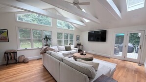 Amplia sala de estar con un sofá modular grande, un ventilador de techo y un televisor montado en la pared.