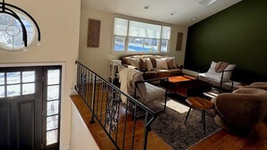 Amplia sala de estar con escalera, un conjunto de sofás, una mesa de centro y vistas al exterior.