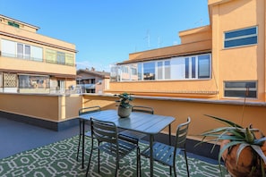 A rooftop terrace with a table and chairs, a potted plant, and a view of neighboring buildings. - Spacious bright and cozy penthouse with terrace close to metro station (Roma)