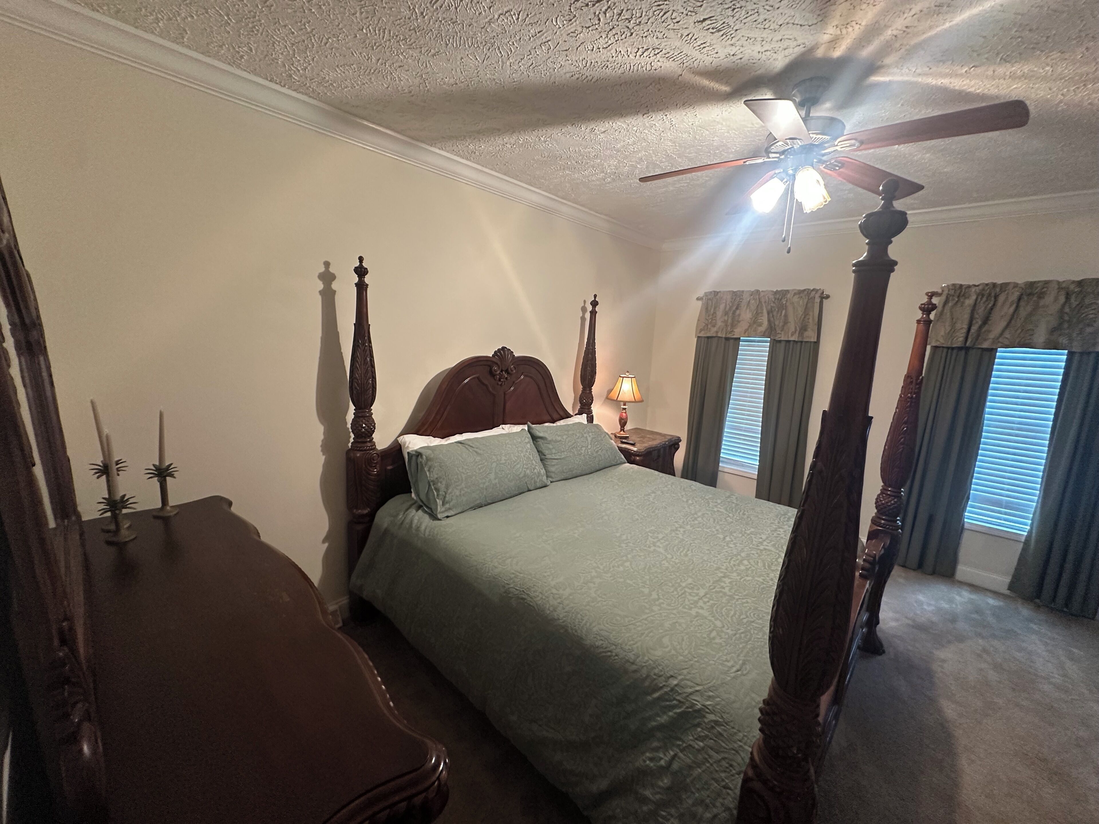 Ein Bett mit Baldachin, ein Holzkopfstück, ein Nachttisch mit Lampe und ein Deckenventilator.