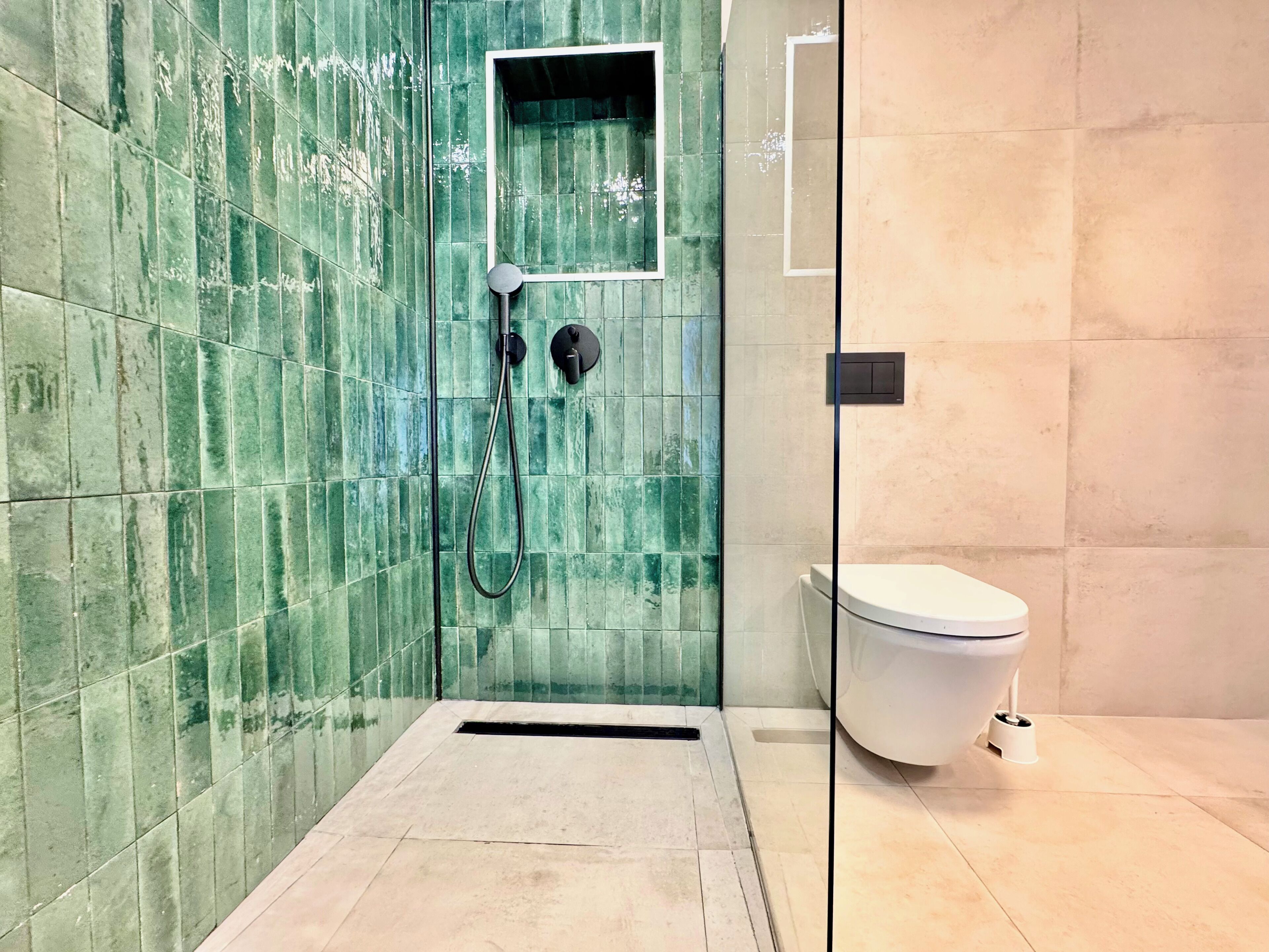 Een badkamer met groen betegelde muren, een wit toilet en een douche.