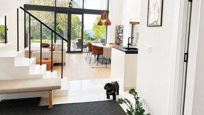 Een modern interieur met een trap naar een eetgedeelte en keuken, grote ramen, en een zwarte hond.