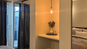 A bedroom with a bed, a small stool, a nightstand with a plant, a hanging light, and a sliding door leading to an outdoor area.
