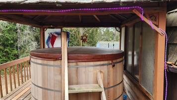 A wooden hot tub with a wooden deck and a covered area with purple LED lights.