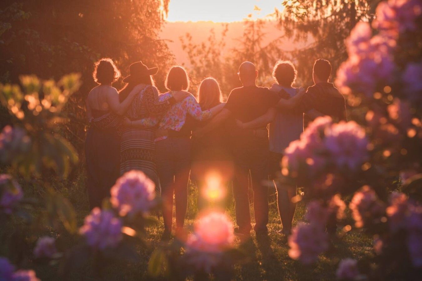 A group of people standing in a field with a sunset in the background.