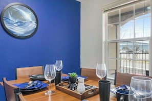 Un comedor con pared azul, un espejo redondo y ventana con vista a un estacionamiento.