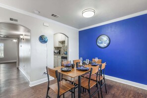 A dining area with a wooden table set for four, a kitchen in the background, and a blue accent wall. - Stadium View Balcony | Walk to AT&T + Globe Life! (Arlington)