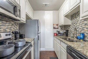 Una cocina con armarios blancos, un refrigerador de acero inoxidable, un microondas, una estufa y una encimera de granito.