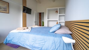 Quarto com cama, televisão fixada na parede, cabeceira de madeira e guarda-roupa branco.