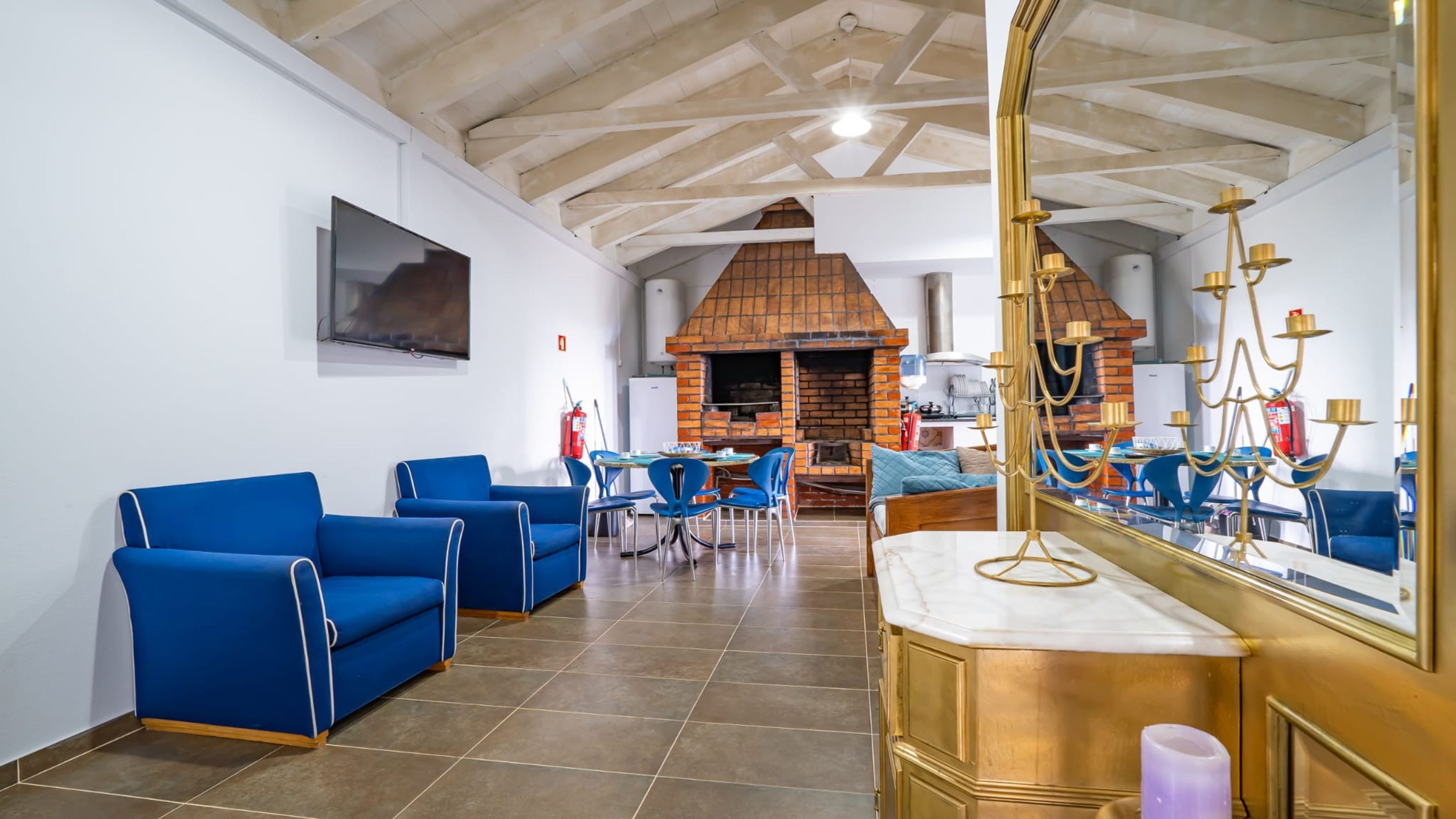 Amplia habitación con sofás azules, un espejo grande, chimenea y suelo de baldosas.