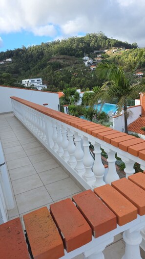 A balcony with a white balustrade and red bricks, overlooking a pool and a hillside with houses. - Ocean Heated Pool Jacuzzi View II Flat (Santa Cruz)
