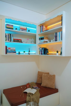 Ein Zimmer mit Bücherregal, einer Leseecke mit rotem Sofa und einer Wandablage mit Büchern und dekorativen Gegenständen.