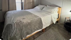 A bedroom with a bed, curtains, a window, a bedside table, and a rug.