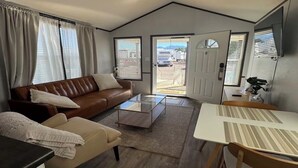 A compact living space with a sofa, a coffee table, a dining table with chairs, and a door leading outside.