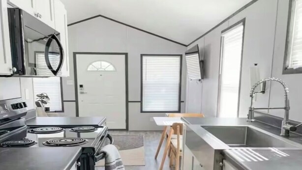 A modern kitchen with stainless steel appliances, a wooden dining table, and a large window.