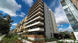 Un immeuble moderne à plusieurs étages, doté de balcons, avec un ciel dégagé et entouré de verdure.