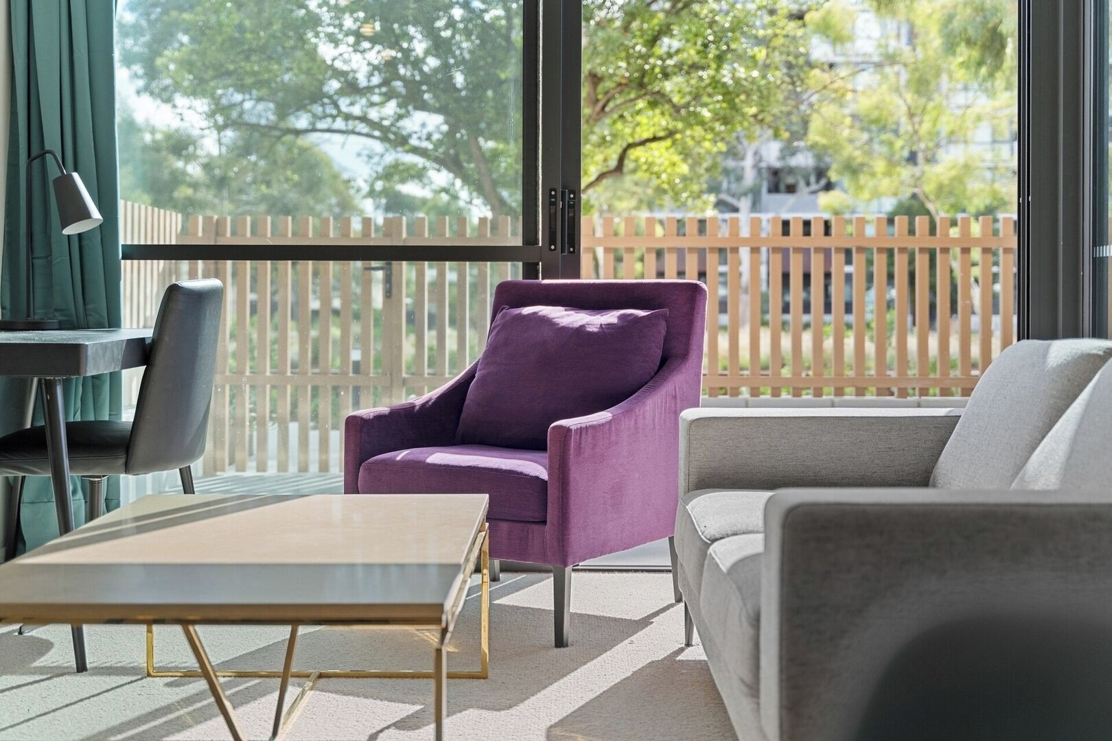 Una sala de estar moderna con un sillón morado, un sofá gris y una mesa de centro de madera.