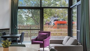 Une pièce moderne avec une grande fenêtre, une table ronde, un fauteuil violet et un canapé gris.