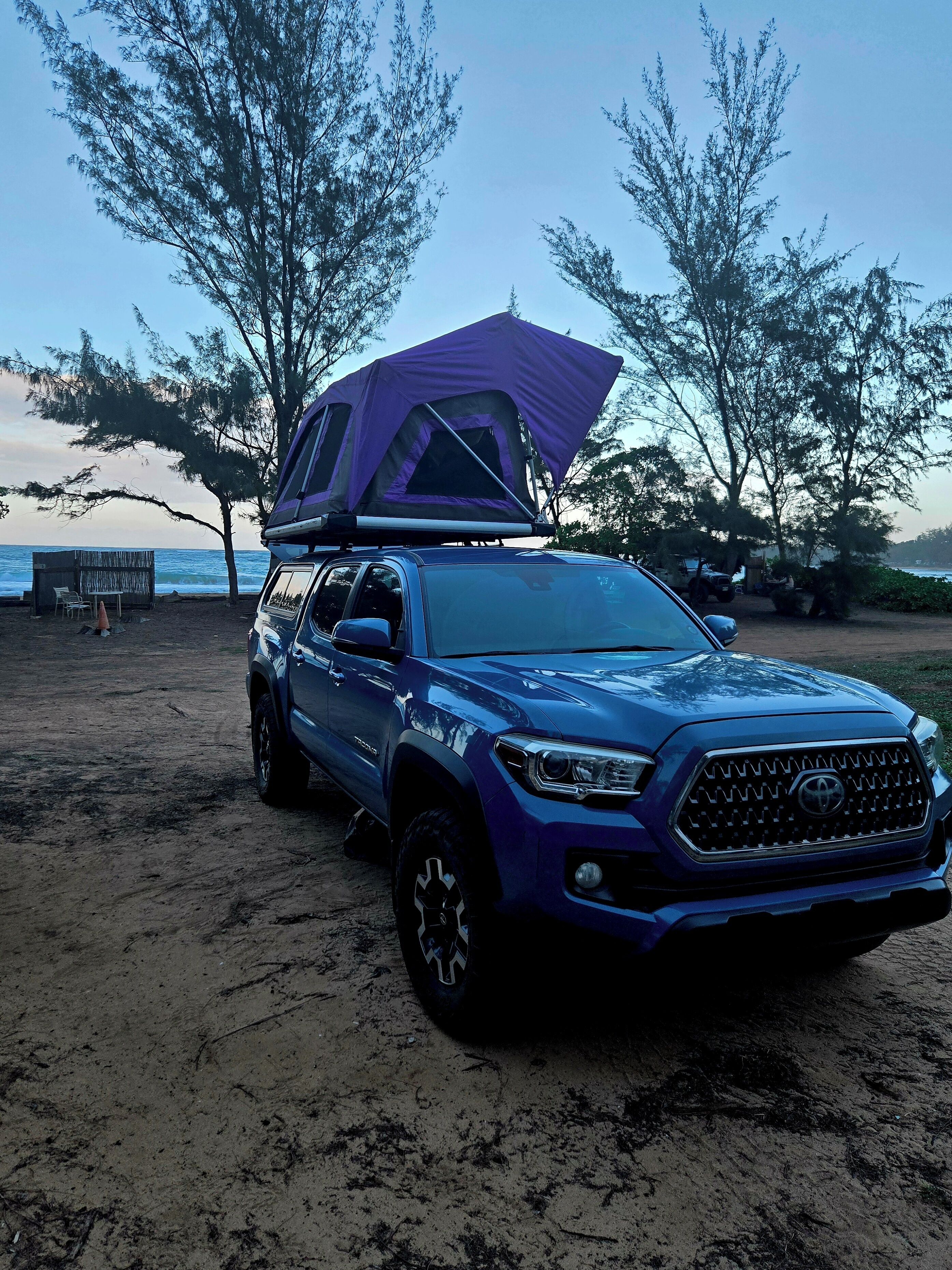 A blue SUV with a purple tent on the back parked on a sandy beach.