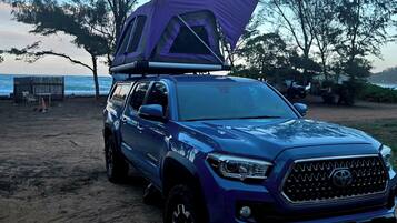 A blue SUV with a purple tent on the back parked on a sandy beach.