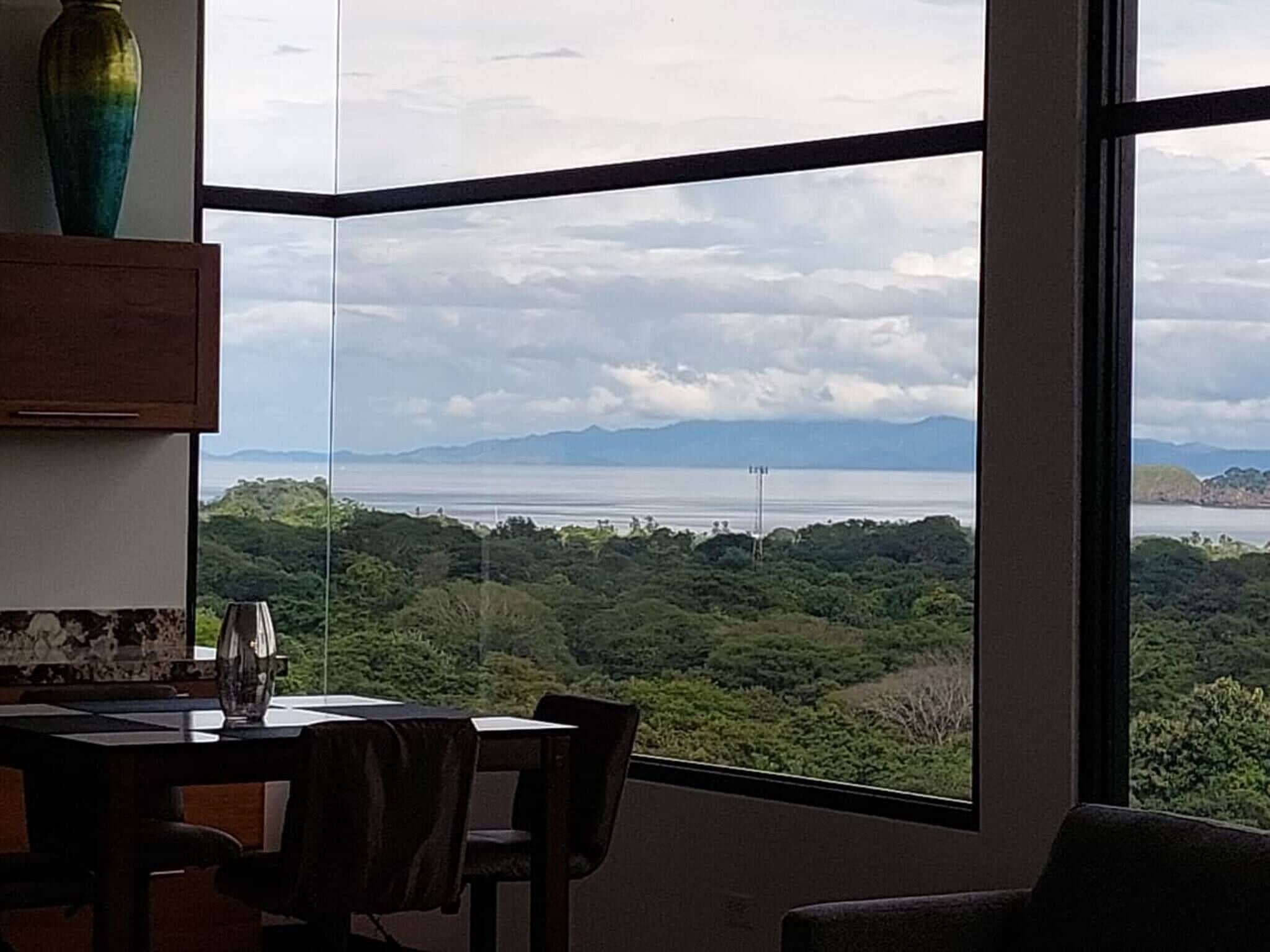 A room with a large window offering a view of a coastal landscape with mountains.