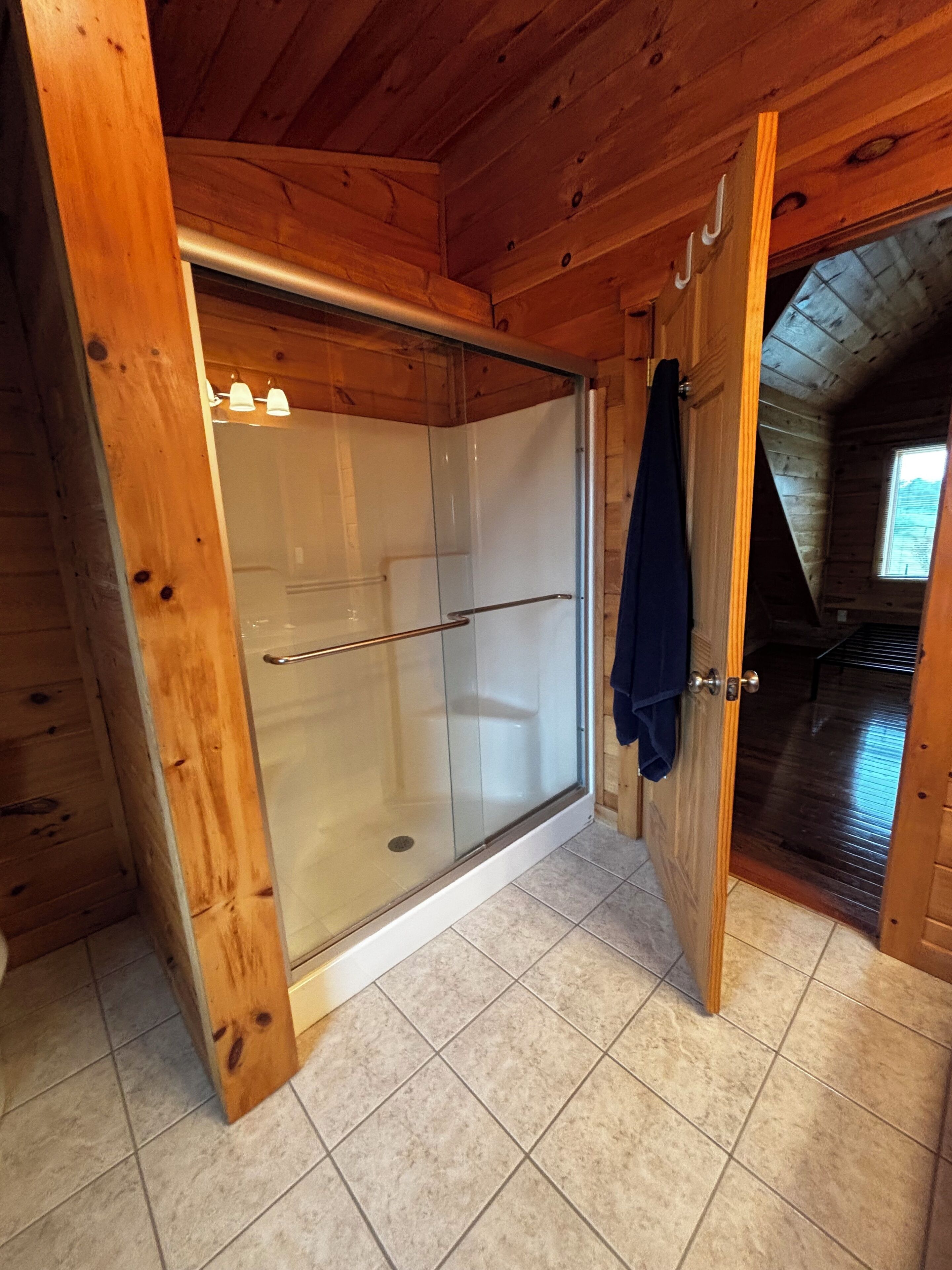 A wooden cabin with a glass shower enclosure, a tiled floor, and a door leading to another room.
