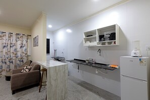 A compact kitchen with a marble countertop, a refrigerator, and a built-in shelf unit. - Laize & Lucas Residential - 102 - Comfort Minutes from the Beach (Aracaju)