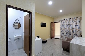 A room with a bathroom, a desk, a chair, a television, and a curtain. - Laize & Lucas Residential - 102 - Comfort Minutes from the Beach (Aracaju)