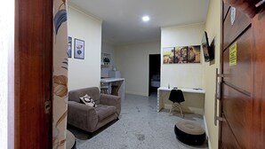 Ein kompakter Wohnbereich mit Sofa, Schreibtisch, Stuhl und Gitarre.
