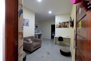 A compact living space with a sofa, a small desk, a chair, and a guitar. - Laize & Lucas Residential - 102 - Comfort Minutes from the Beach (Aracaju)