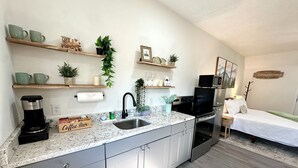 A modern kitchen with a coffee maker, microwave, and oven. There are shelves with plants and a bed in the adjacent room. - Romantic King Bed, Heart Shaped Hot Tub, Fire Pit (Zaleski)