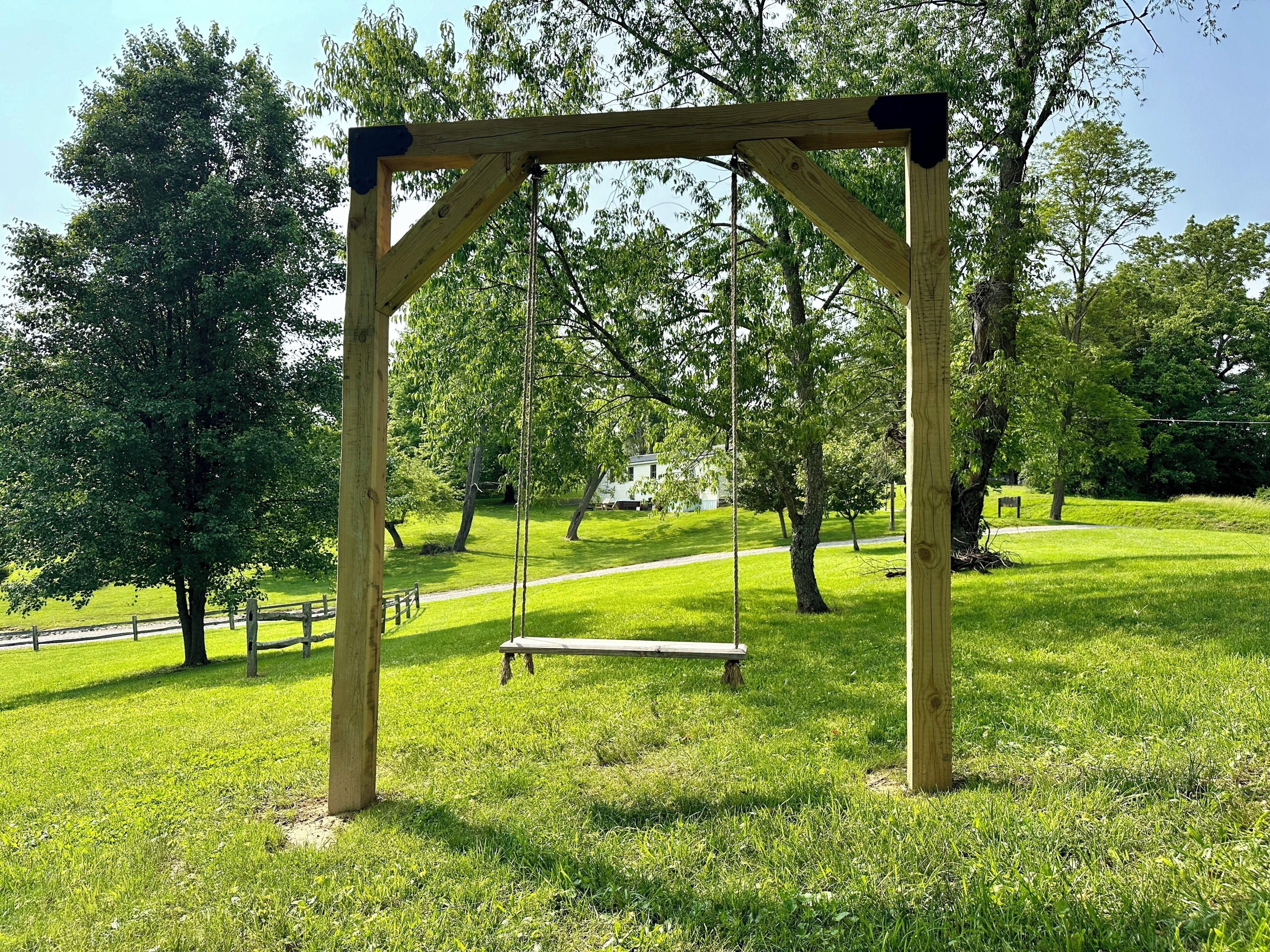 Een houten schommel in een park met gras en bomen.