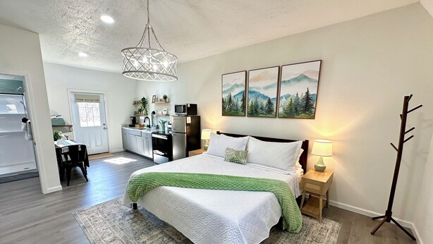 A modern bedroom with a large bed, a dining area, and a kitchen in the background. - Romantic King Bed, Heart Shaped Hot Tub, Fire Pit (Zaleski)