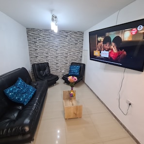 Un saló amb dos sofàs de pell negra, una taula de centre de fusta amb un ram de flors, una televisió de pantalla plana penjada a la paret i un mur amb un disseny decoratiu.