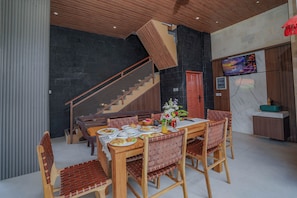 Un comedor con una mesa y sillas de madera, una escalera y un televisor fijado a la pared.