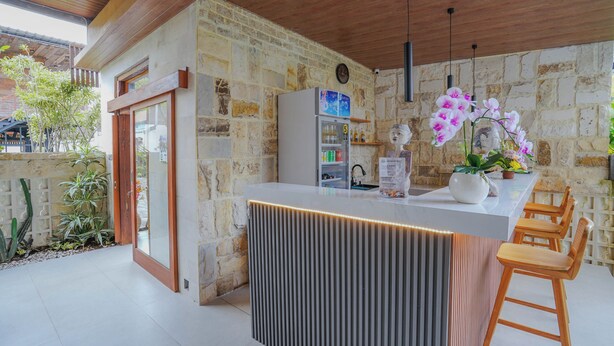 Une cuisine moderne dotée d’un réfrigérateur encastré, de tabourets de bar en bois et d’une plante orchidée en pot.