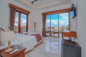Una habitación de hotel con cama, escritorio, televisor y ventanas amplias.