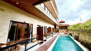 Un espace aménagé au bord de la piscine, avec une terrasse en bois, une piscine et un bâtiment doté de nombreuses fenêtres et portes.