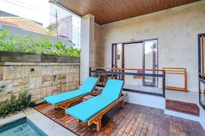 Zona de piscina con dos sillones de madera y un muro de piedra.