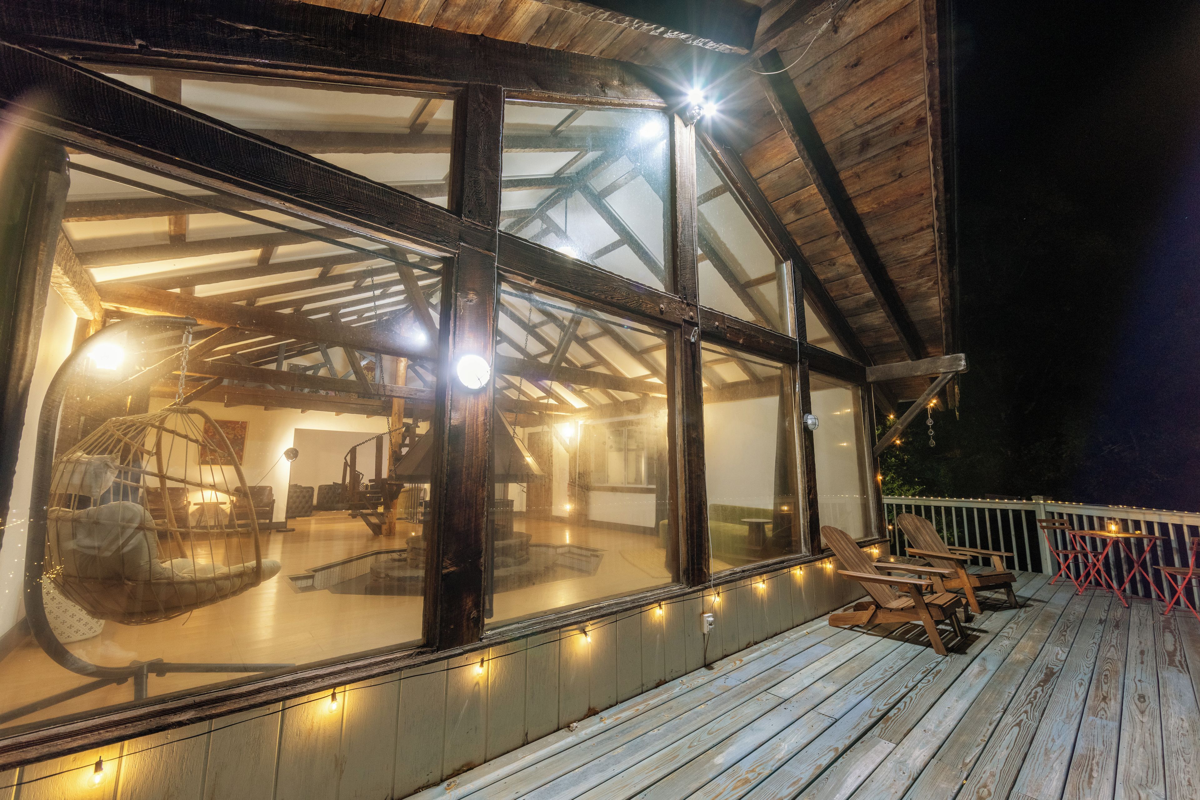 A wooden deck with outdoor seating and a glass enclosure with interior lighting.