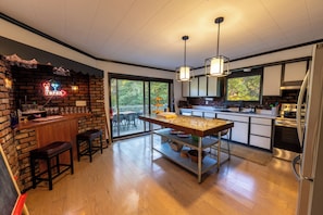 A modern kitchen with a central island, bar area with stools, and large windows offering a view of the outdoors. - Private River Access • One-of-a-Kind Firepit Lounge • Catskill• NYC 2hr Getaway (Roscoe)