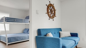 A room with a bunk bed, a blue armchair, and a ship's wheel decoration. - Coastal Cottage STEPS to BEACH and downtown Old Orchard Beach - Prime Location (Old Orchard Beach)